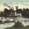 Steamboat on river with tree-lined shoreline in background