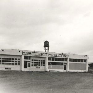 Single story white concrete block building with water tank on top with "Masterfit Manufacturing Corporation" on the front