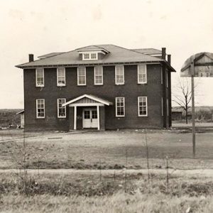 Multiple story brick building flanked by two single story wooden buildings