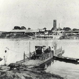 Horse and buggy on ferry; town visible across river