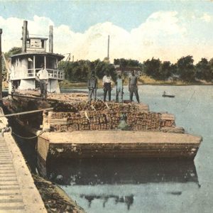 Men standing on barge in front of steamboat beside railroad tracks and train