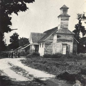 Small group of children alongside wooden building with bell tower