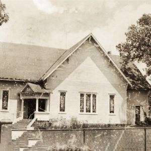 Single story white building behind chain link fence