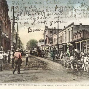 Large crowd of people on street with horses and wagons and multistory storefront buildings on both sides