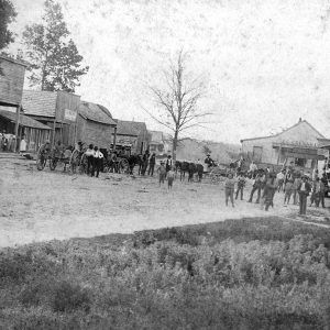 People standing in dirt road between two rows of wooden buildings