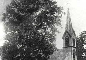 Wooden church building with large spire with cross on top