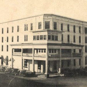 Multistory white brick building with cars parked adjacent