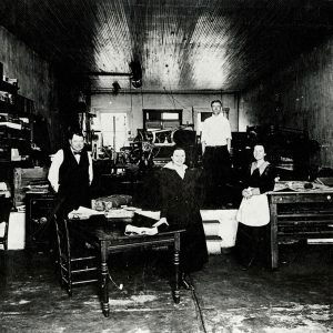 Two white men and two white women in newspaper printing office