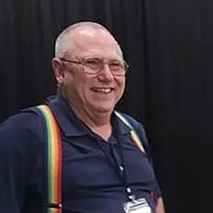 White man in blue short-sleeved shirt and rainbow suspenders