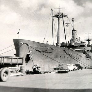 Side view of long ship docked with cars in the foreground