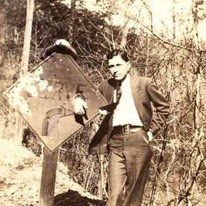 White man in suit and tie posing by road sign saying "curve"