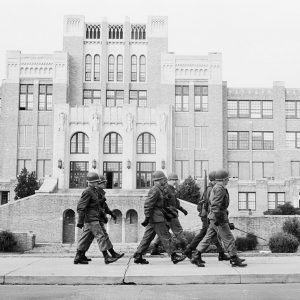 Soldiers in uniform marching in front of multistory school complex