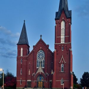 Multistory red brick church building with two spires of different heights