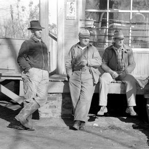 Four white men in hats lounging on porch of store