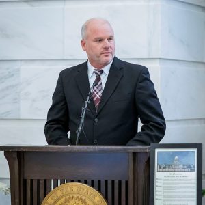 White man in suit and tie at lectern