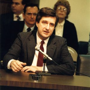 White man in suit and tie being emphatic at microphone