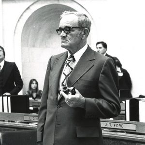 White man with glasses in suit and tie holding a pipe