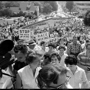 Large crowd of white people listening to talk with some holding signs saying "Stop the Race Mixing"