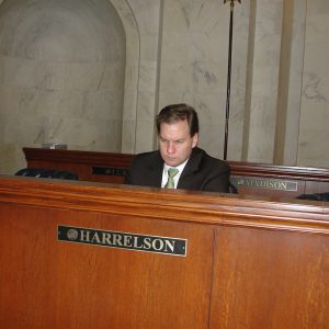 White man in suit and tie looking down and scowling