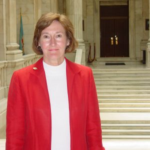 White woman in red suit jacket over white top