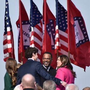 white woman in a hot-pink suit standing next to a white man in a suit and a black man in judge's robes