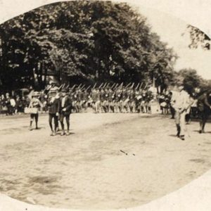 Soldiers with guns at rest on their shoulders marching down town street