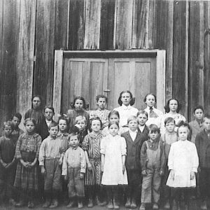 Group of school children gathered in front of wooden building