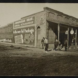 People standing on street next to row of buildings with ads painted on the sides