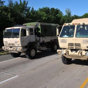 Two military vehicles parked on road near flooded section