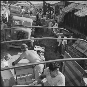 people loading trucks and standing outside barracks building