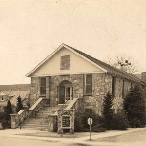 multistory stone church building with steps leading to the front door next to stone house