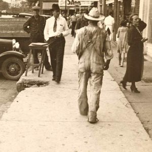 people walking along sidewalk with storefronts and vehicles