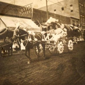 Two white women in decorated horse-drawn carriage proceeding down town street