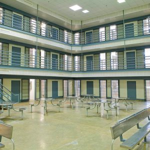 Interior of a prison showing three floors of cells and a center area with metal tables and benches