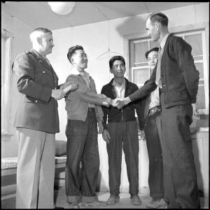 White man shaking young Asian man's hand with another white man and other Asian young men standing with them