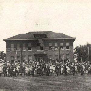 Large group of people gathered in front of multistory brick building