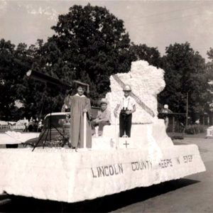 Three kids sitting and standing on parade float dressed as a cowboy