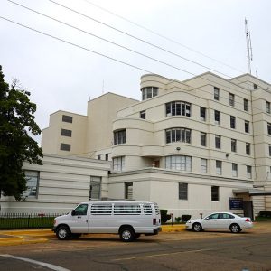 multistory modern building with a white van and white car parked by it