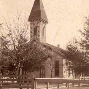 multistory wooden church building with fence around it and a tall spire