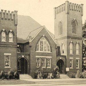 Multistory brick church building with arched and stained glass windows and tower