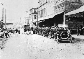 Line of cars and buildings; musicians walking in street