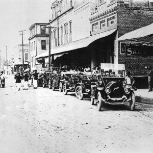 Line of cars and buildings; musicians walking in street