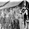 Group of white people standing and three white men on horses holding rifles