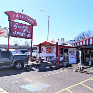 Cars parked beneath awning next to metal building with big red sign saying "Ed Walkers French dipped sandwiches"