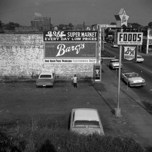 Multistory brick building with parking lot with sign saying "Goff Supermarket" and other signs