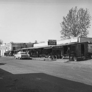 Car parked in front of series of low buildings with people beneath an awning