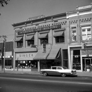 Different storied storefront buildings with car parked at curb in front