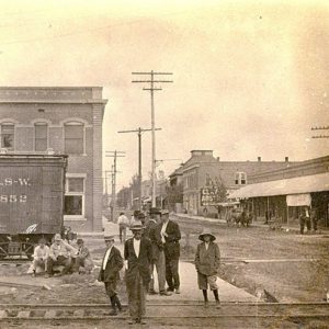 people standing near train tracks with rail car and town buildings in background