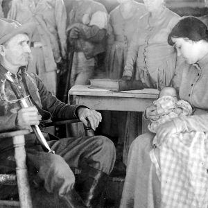 White man holding knife while sitting; white woman holding baby while sitting