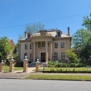 Multistory blond brick house behind wrought iron fence